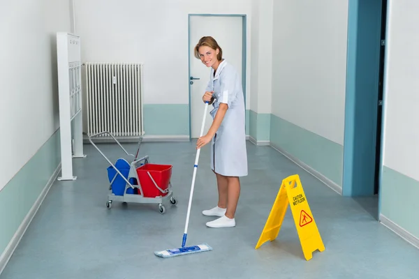 Janitor com sinal de precaução molhada e equipamentos de limpeza — Fotografia de Stock