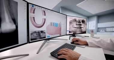 Diş hekimi hastayla bilgisayar ekranında diş röntgeni görüntülerini inceliyor.