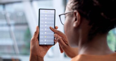 Kadın meteorolog, danışma odasında akıllı telefondan hava durumunu kontrol ediyor.