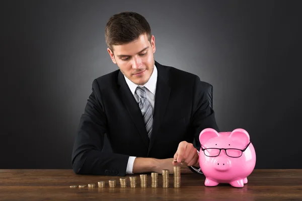 Empresario con Piggybank apilar monedas — Foto de Stock