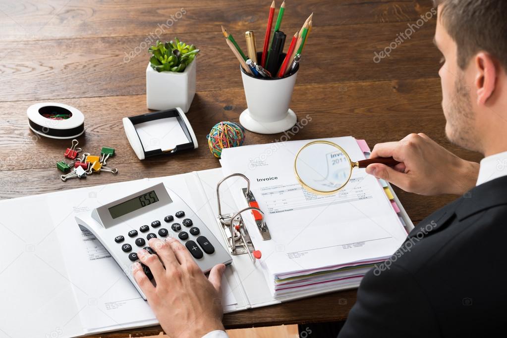 Businessman Inspecting Invoice At Desk