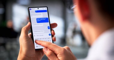 Genç İspanyol adam telefonu tutuyor, mesajları kontrol ediyor, internete e-posta yolluyor. Olası Meslekler: Sosyal Medya Yöneticisi