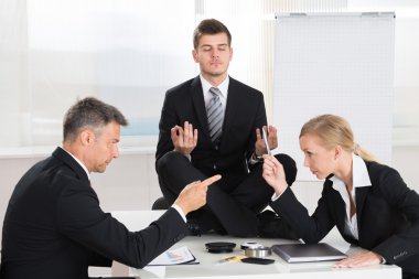 Businesspeople Quarreling In Front Of Businessman Meditating clipart