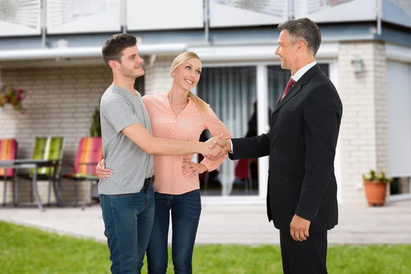 Agente imobiliário agitando as mãos com casal — Fotografia de Stock