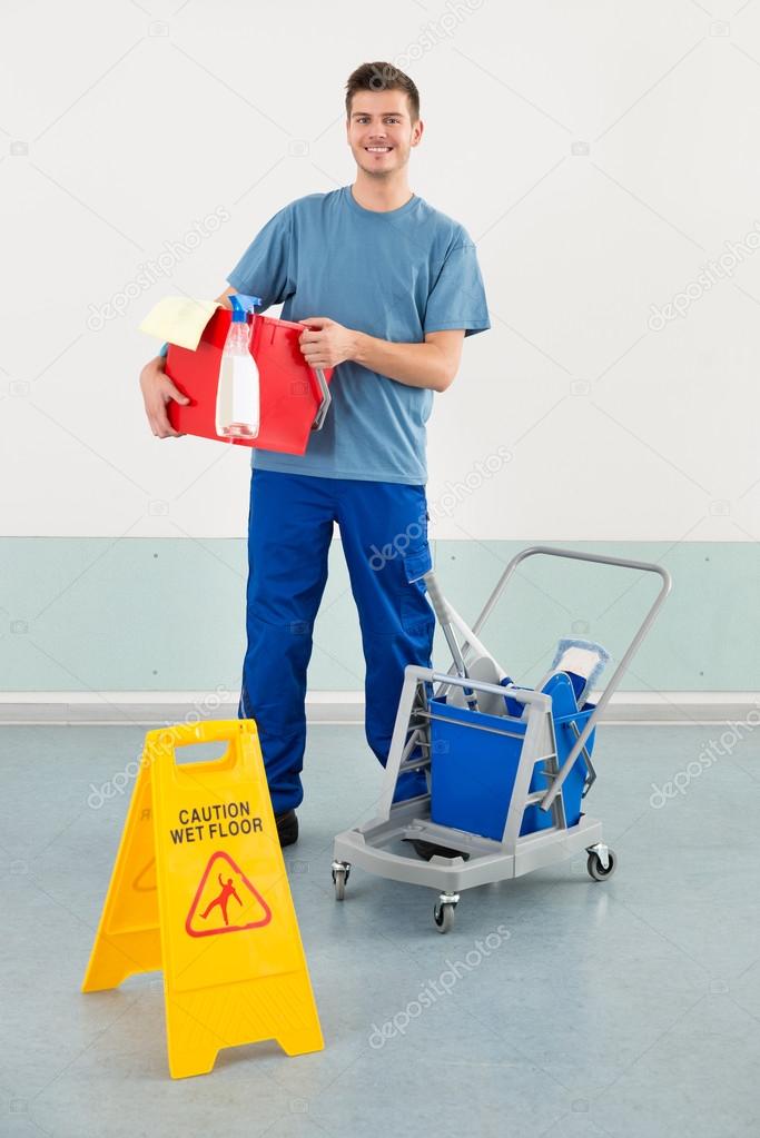 Worker With Cleaning Equipments And Wet Floor Caution Sign