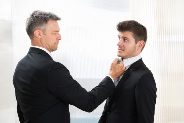 Businessman Holding Young Businessman's Tie clipart