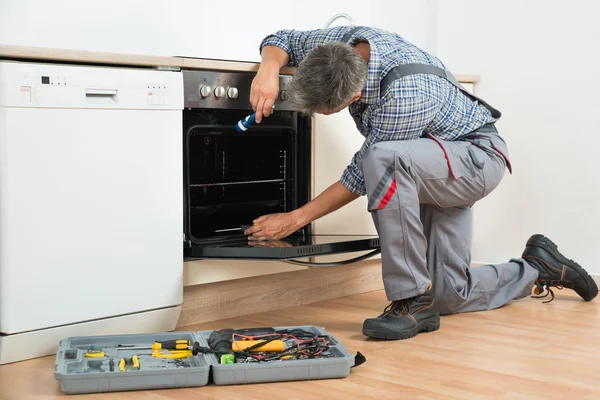 Reparador examinando forno com lanterna — Fotografia de Stock