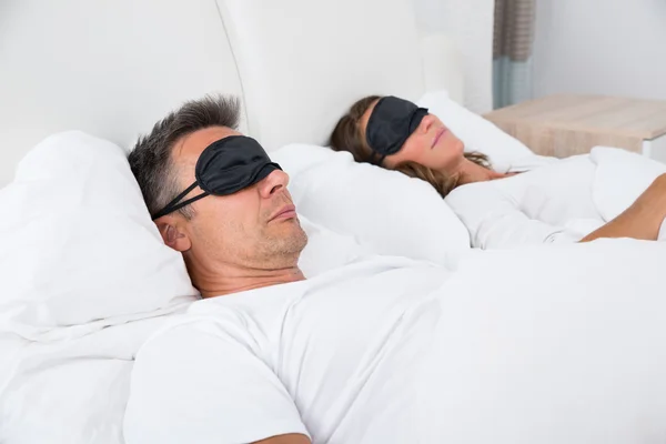 Pareja durmiendo en la cama usando máscara ocular —  Fotos de Stock