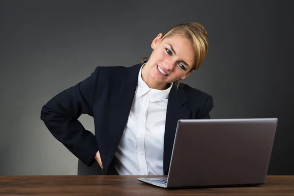 Empresária sofrendo de dor nas costas ao usar laptop — Fotografia de Stock