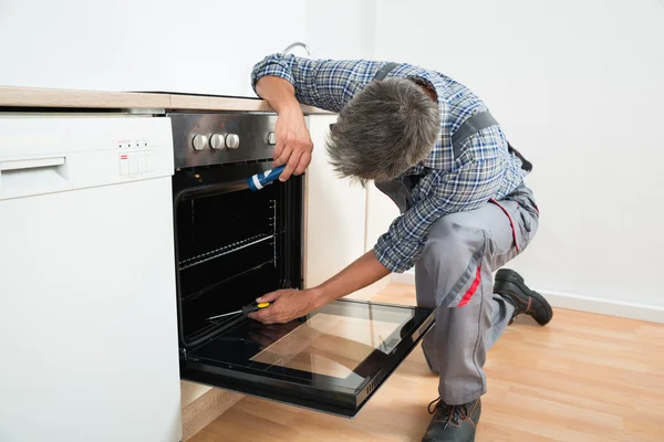 Reparatör undersökande ugn med ficklampa — Stockfoto