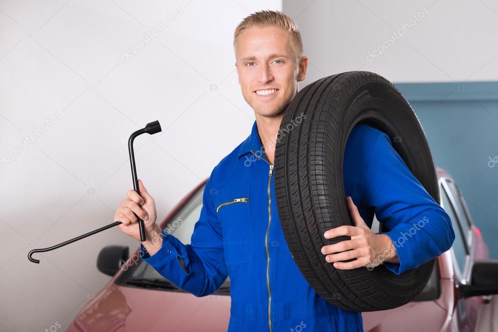 Smiling Mechanic Holding Tire And Wrench