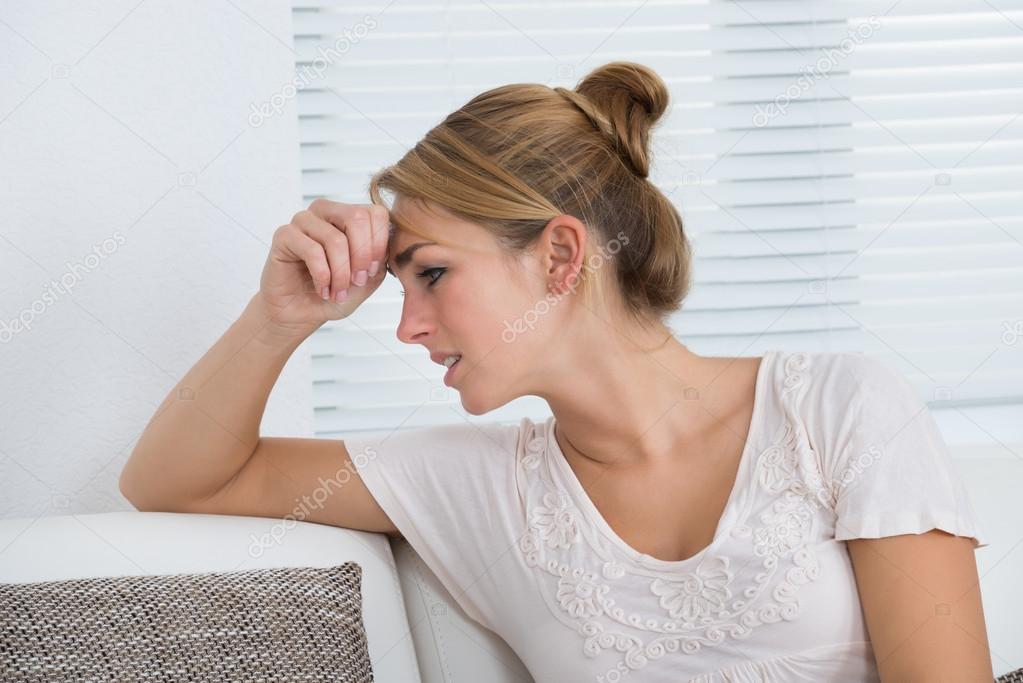Woman Suffering From Headache While Sitting On Sofa