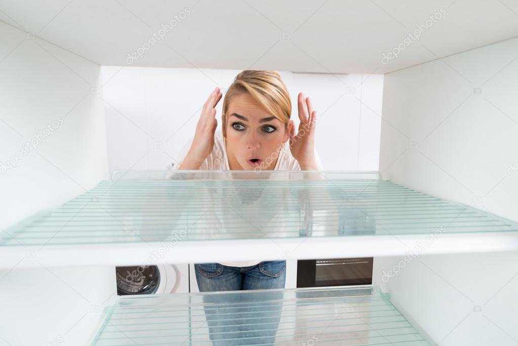 Shocked Woman Looking At Empty Refrigerator
