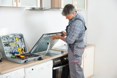 Repairman Examining Stove In Kitchen clipart