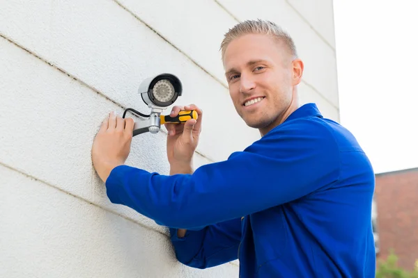 Lächelnder Techniker installiert Kamera an Wand — Stockfoto