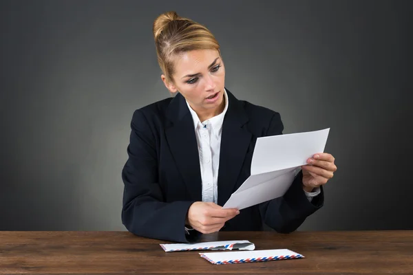 Geschockte Geschäftsfrau liest Brief am Schreibtisch — Stockfoto