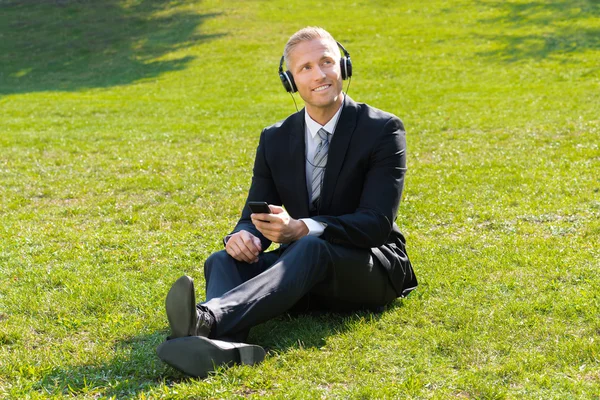 Empresário ouvindo música no parque — Fotografia de Stock