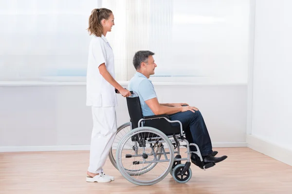 Arzt schiebt behinderten Patienten in den Rollstuhl — Stockfoto