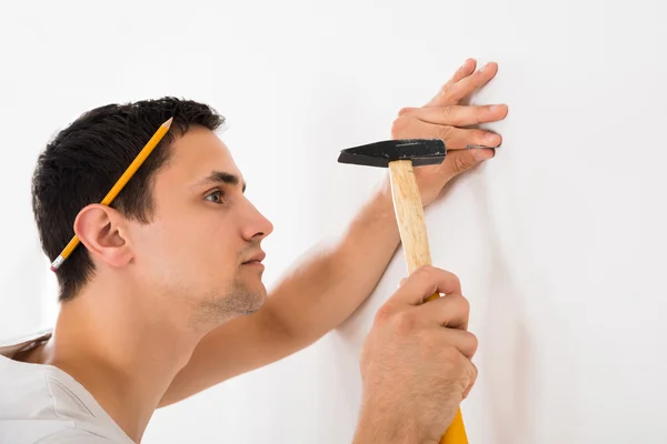 Man hameren spijker op witte muur — Stockfoto