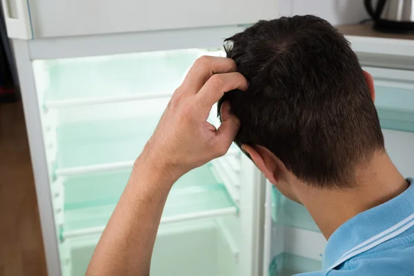 Homem confuso olhando para o refrigerador vazio — Fotografia de Stock