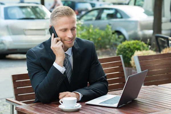 Empresário conversando no celular olhando para o laptop — Fotografia de Stock