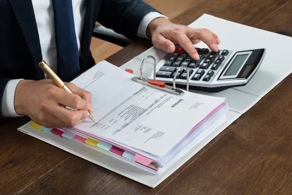 Empresario usando la calculadora mientras revisa la factura —  Fotos de Stock