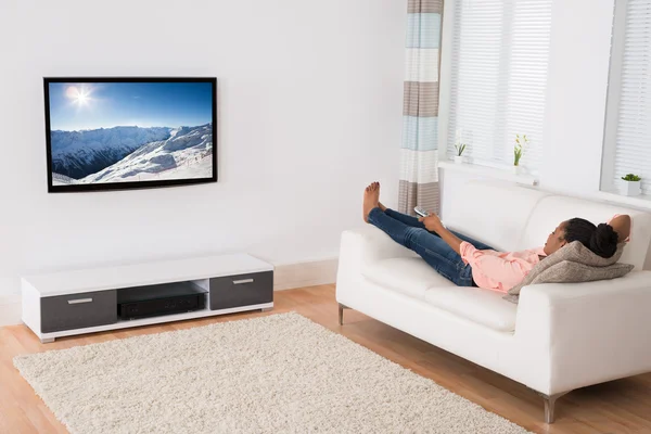 Mujer africana acostada en un sofá viendo televisión —  Fotos de Stock