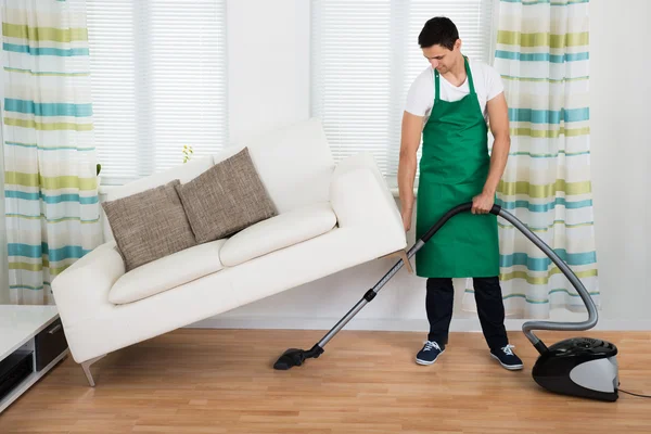 Homem levantando sofá enquanto limpando o chão — Fotografia de Stock