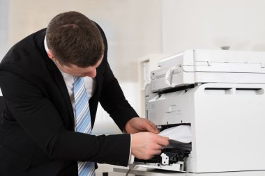 Businessman Removing Paper Stuck In Printer clipart