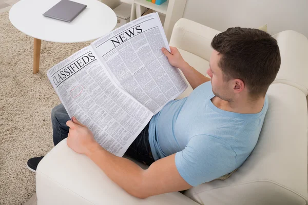 Ο άνθρωπος διαβάζει εφημερίδα στον καναπέ στο σπίτι — Φωτογραφία Αρχείου