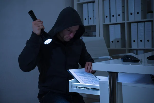 Ladrão com lanterna procurando documentos no escritório — Fotografia de Stock