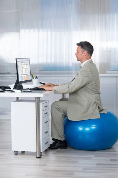 Usando o computador enquanto sentado na bola de exercício — Fotografia de Stock