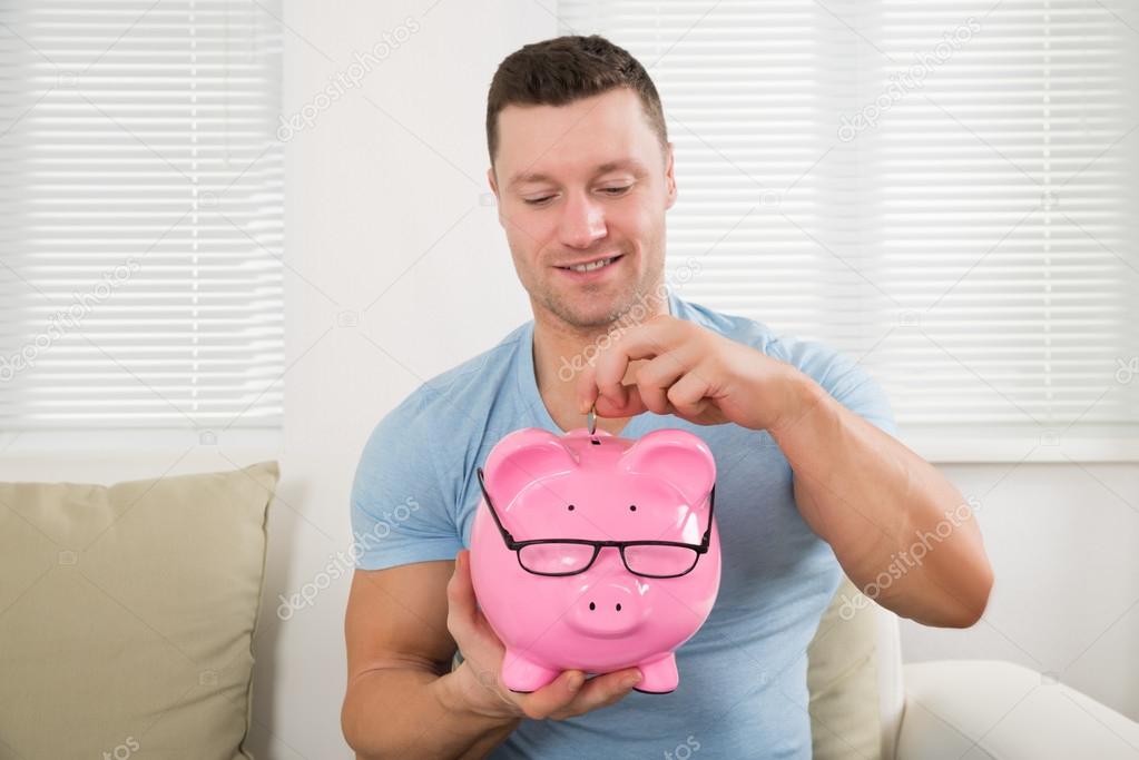 Man Putting Coin Into Piggy Bank