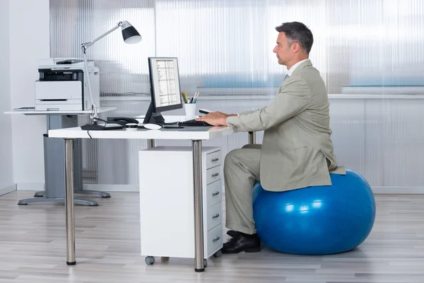 Usando o computador enquanto sentado na bola de exercício — Fotografia de Stock