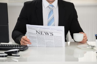 Gazete ve kahve fincanı tutan işadamı