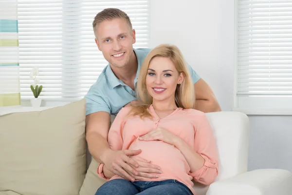 Heureux couple attendu assis sur le canapé à la maison — Photo