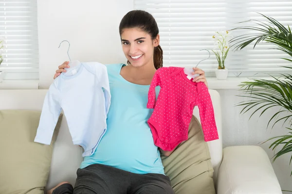 Mulher grávida segurando roupas de bebê — Fotografia de Stock