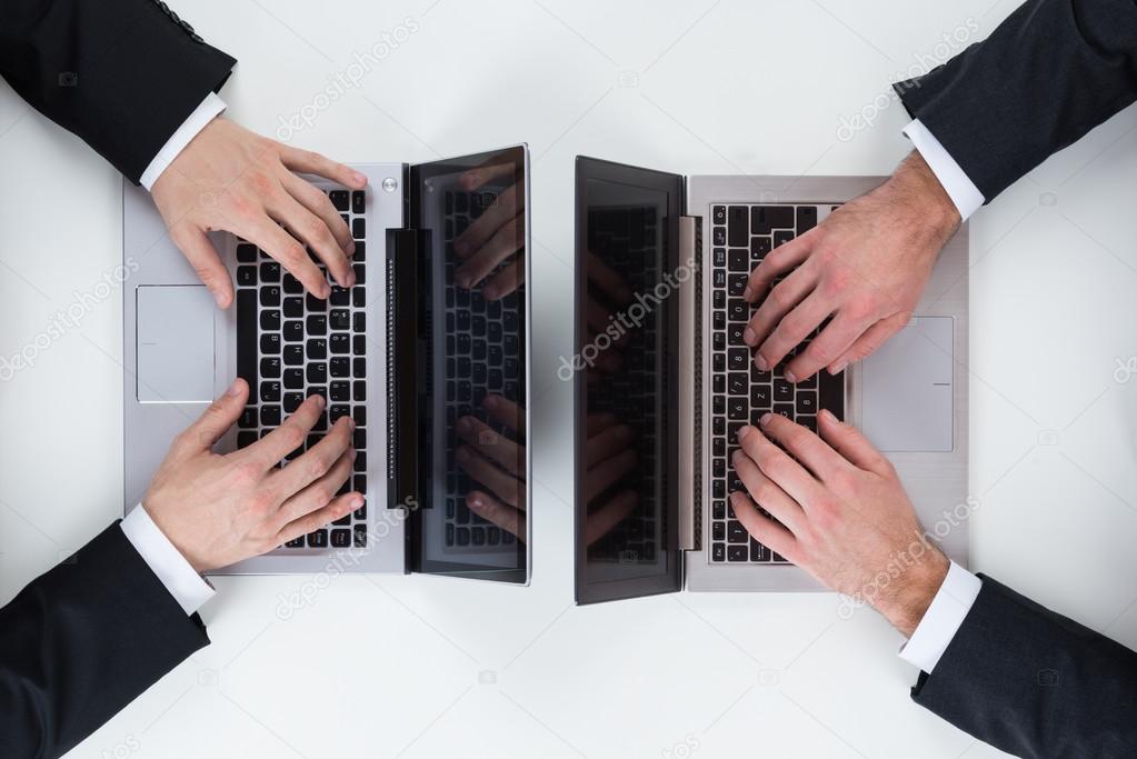 Businessmen Using Laptops At Table In Office