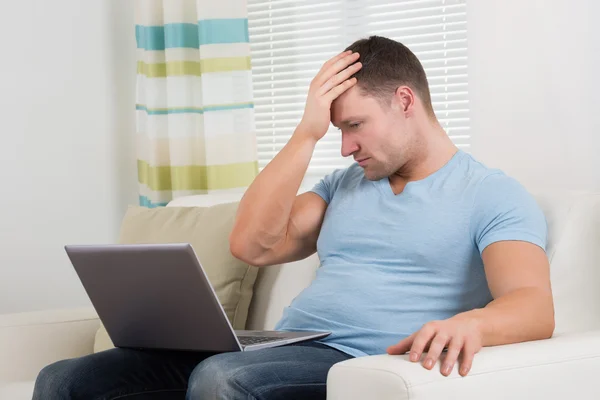 Homem perturbado com laptop sentado no sofá — Fotografia de Stock