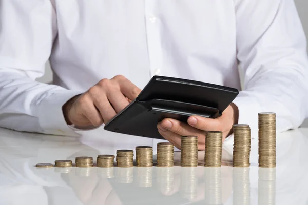 Empresario usando calculadora con monedas apiladas — Foto de Stock