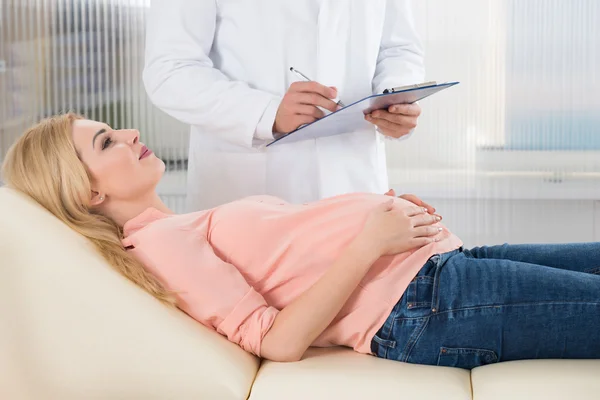 Doctor escribiendo notas por mujer embarazada — Foto de Stock