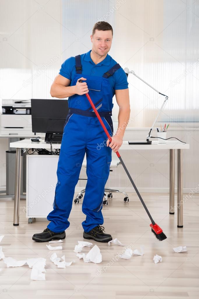 Smiling Janitor Holding Broom In Office