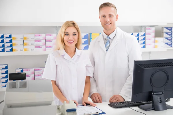 Farmacéuticos sonriendo en contador en farmacia —  Fotos de Stock