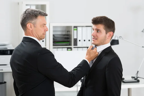 Зрелый бизнесмен цепляется за галстук сотрудника — стоковое фото