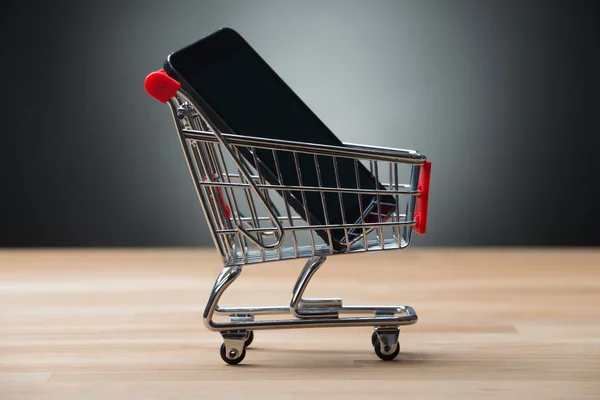 Smartphone v nákupní košík na stole — Stock fotografie