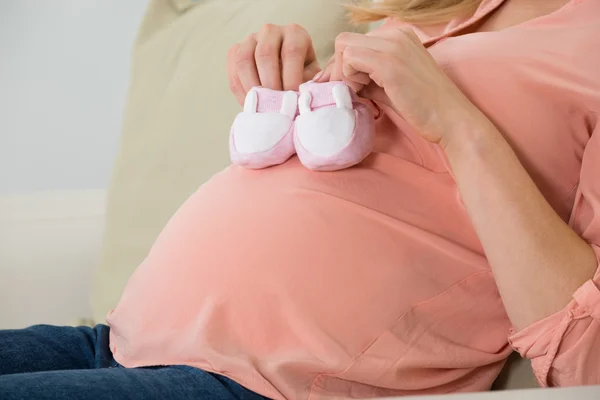 Mujer embarazada sosteniendo zapatos de bebé — Foto de Stock