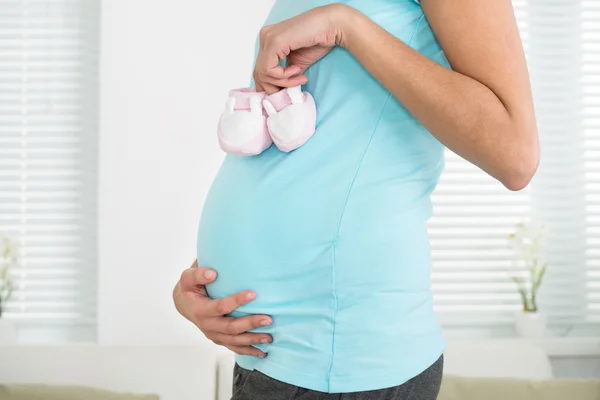 Mujer embarazada sosteniendo zapatos de bebé — Foto de Stock