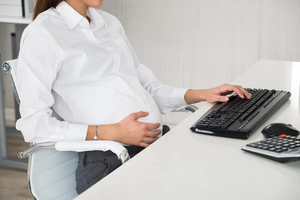 Embarazada mujer de negocios utilizando la computadora en el escritorio —  Fotos de Stock