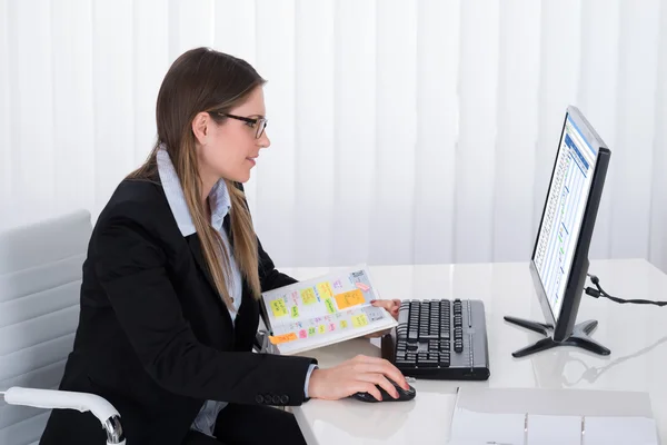 Affärskvinna med dagbok tittar på en dator — Stockfoto