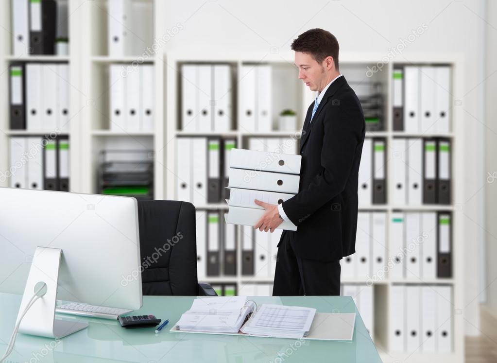 Businessman Carrying Binders By Desk